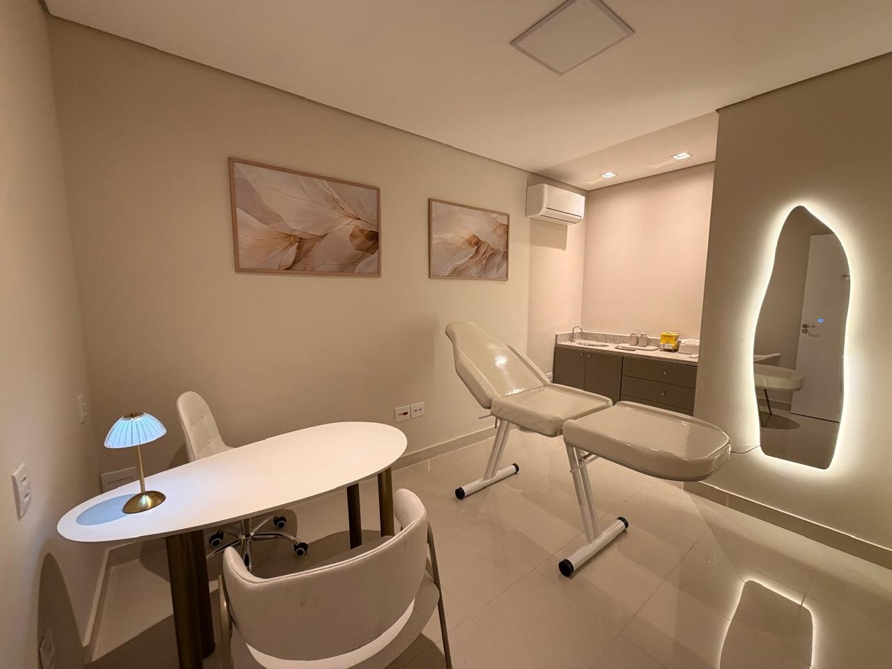 Sala 04: consultório com maca, mesa oval com abajur, cadeiras e espelho com iluminação de LED